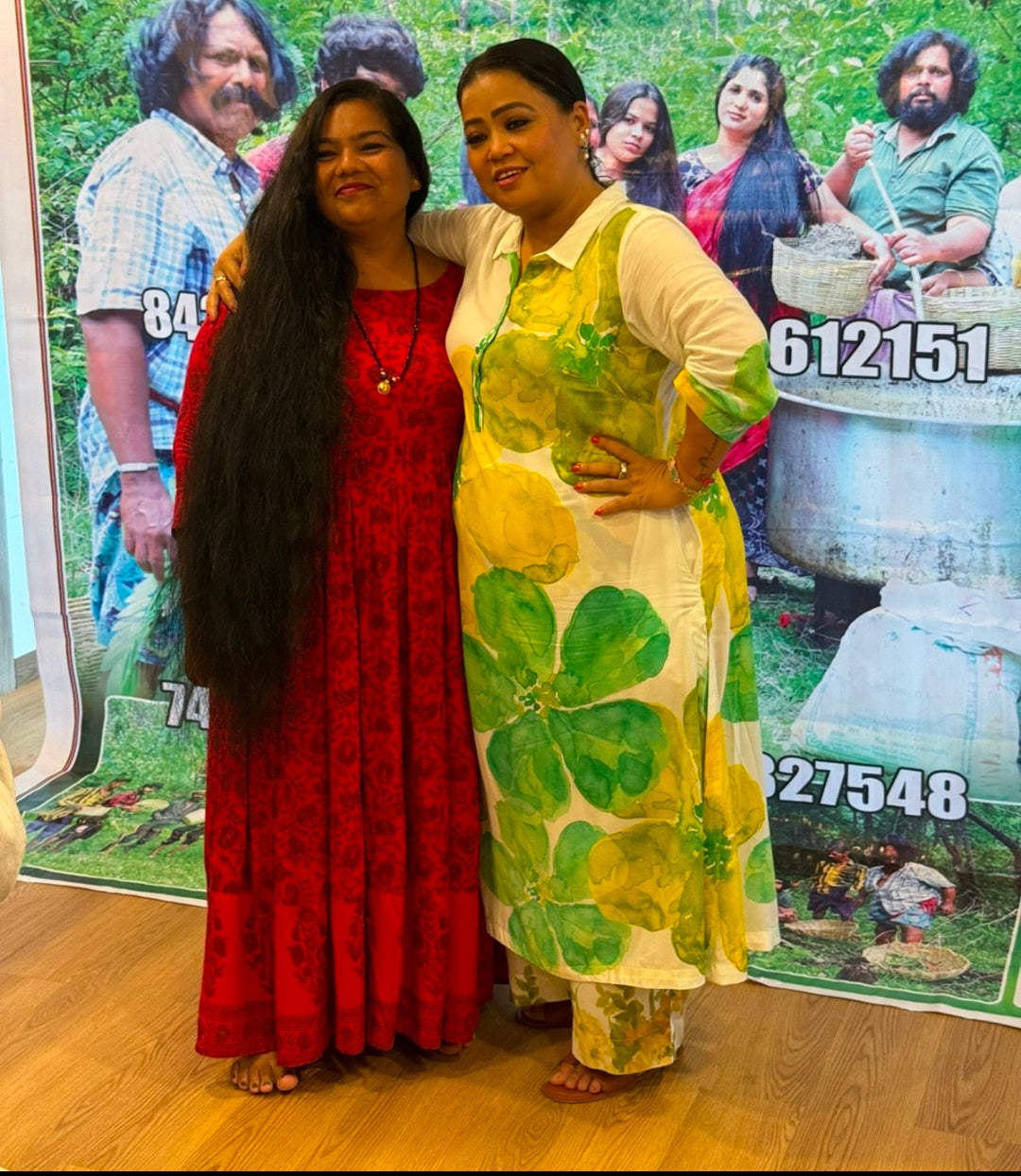 Two women standing in front of a colorful advertisement poster.