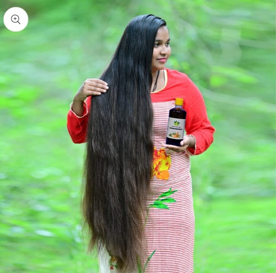 Woman with long hair holding a  HAKKI PIKKI ADIVASI HERBAL HAIR OIL
bottle outdoors