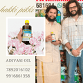Two men holding Adivasi oil bottles with promotional text and contact numbers.