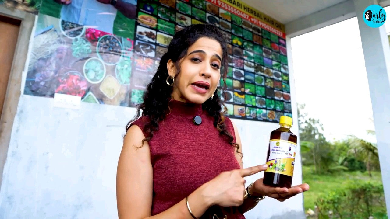 Woman holding a bottle,  HAKKI PIKKI ADIVASI HERBAL HAIR OIL
standing in front of a colorful wall display.
