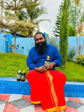 Man in blue shirt and red pants sitting outdoors with bottles on a colorful mat